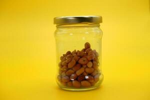 Half filled closed glass jar with peeled nuts isolated on yellow background. photo