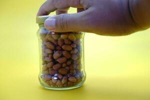 glass jar full of shelled peanuts. hand holding a glass jar filled with nuts photo