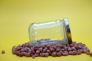 empty glass jar on a pile of peeled nuts isolated on yellow background photo