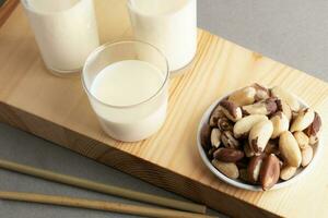 Vegan organic milk replacer made from brazil nuts in glasses, nuts plate on wooden board close up. photo
