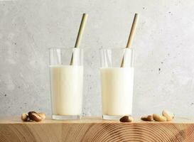 Vegan milk made of brazil nut in two glass with bamboo drinking straws and nuts on wooden table. photo