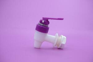 closed faucet isolated purple background. the faucet is white with a purple lid photo