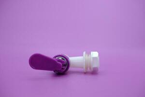 closed faucet isolated purple background. the faucet is white with a purple lid photo