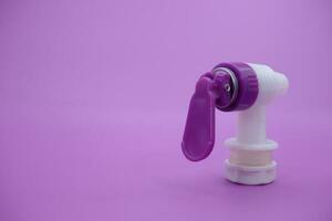 closed faucet isolated purple background. the faucet is white with a purple lid photo