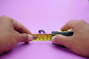 hand holding tape measure isolated purple background. measuring tool used by builders. photo