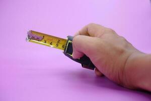 hand holding tape measure isolated purple background. measuring tool used by builders. photo