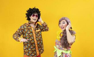 Asian hippie couple dress in 80s vintage fashion with colorful retro clothing while dancing together isolated on yellow background for fancy outfit party and pop culture concept photo