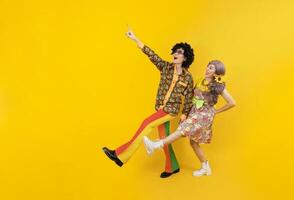 Asian hippie couple dress in 80s vintage fashion with colorful retro clothing while dancing together isolated on yellow background for fancy outfit party and pop culture concept photo