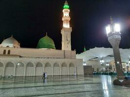 Medina, Saudi Arabia, May 2023 - Beautiful night time view of Masjid Al Nabawi, Medina. Visitors, courtyards outside the mosque, beautiful lights and electronic umbrellas can also be seen. photo