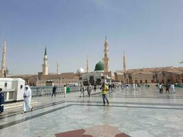 Medina, Saudi Arabia, May 2023 - A beautiful daytime view of Masjid Al Nabawi, Medina's outer courtyard, pilgrims and mosque canopies. photo