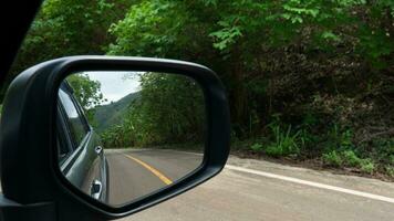 espejo ver de gris coche viaje en el asfalto la carretera. con borroso de verde bosque junto a la carretera a día. foto