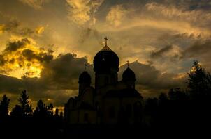 The silhouette of the domes of an Orthodox Christian church in Romania against the background of the red sky. Faith or religion concept photo