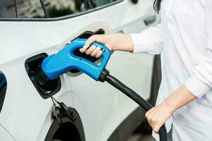 joven negocio mujer repostaje su eléctrico coche a un ev cargando estación. concepto de ambientalmente simpático vehículo. eléctrico coche concepto. verde de viaje. foto