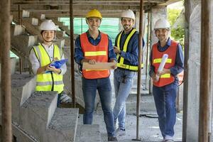 Portrait of experienced diversity team of engineer, architect, worker and safety manager smiling together at the construction site in safety vest and helmet photo