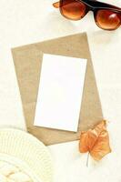 Invitation or greeting card mockup with dry leaf, sunglasses and woolen cap decorations. photo