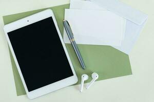 Tablet, earphone, card, envelope and pen on green and white background. Communication concept. photo