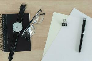 Notebook, pen, eyeglasses and papers on wooden desk overhead view. photo