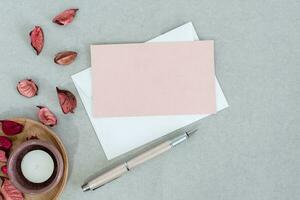 Empty pink card with white envelope, candle and petals, on gray background. photo