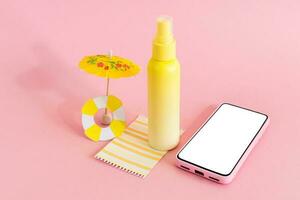 Assembling the skin care cream bottle container, beach umbrella and smart phone on pink background. Summer travel and vacation concept. Beauty and cosmetics concept. photo