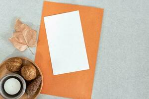 Blank greeting or invitation card mockup with dry leaf and candle, on gray desk. photo