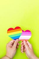 Two hands holding a heart painted like a gay and lesbian flag, isolated on a green background. photo