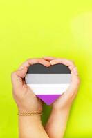 Woman hands hold heart in the colors of asexual flag on green background. LGBT concept, Pride month. Top view, copy space. photo