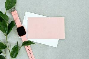 Top view of empty pink card with white envelope, watch and leaves, on gray background. photo