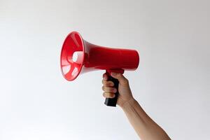 The hand holds a blue megaphone on red background. Announcement concept. Shout It Out. photo