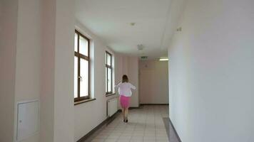 joven mujer en un brillante rosado vestir y blanco cárdigan en un corredor caminando lejos video