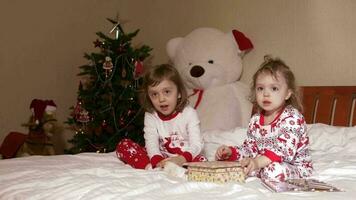 Children dressed in Christmas pajamas are playing with wooden box on the bed video