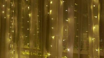 Little boy in christmas pajamas standing behind the curtain decorating the window with christmas ornaments and christmas light video