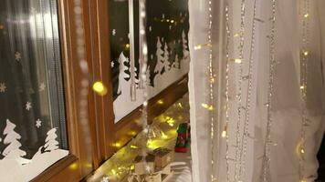 Little boy in christmas pajamas standing behind the curtain decorating the window with christmas ornaments and christmas light video