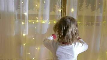 Little boy in christmas pajamas decorating curtain with christmas light beside the christmas tree video