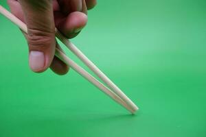 hand holding a pair of chopsticks isolated on green background. photo