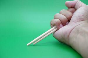 hand holding a pair of chopsticks isolated on green background. photo