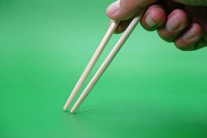 hand holding a pair of chopsticks isolated on green background. photo