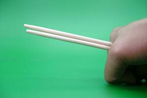 hand holding a pair of chopsticks isolated on green background. photo