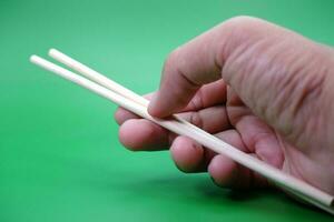 hand holding a pair of chopsticks isolated on green background. photo