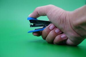 hand holding stapler isolated on green background. photo