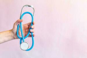 Female hand holds a stethoscope on a light pink isolated background. photo