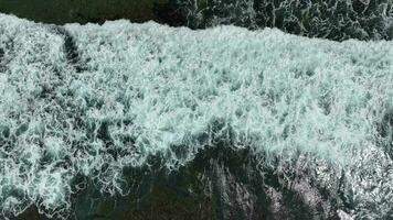 Aerial view of dark ocean waves with white wash. Brown reef with azure water covered by waves crashing into white sea foam. video