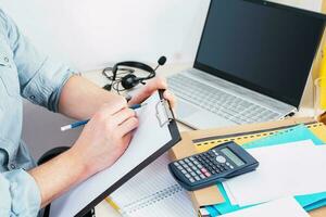 Man working from home office taking reading and writing notes in note pad while working on laptop computer casual businessman entrepreneur. photo