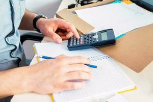 ver de masculino manos contador auditor haciendo papeleo a escritorio lleno de financiero documentos controlar contabilidad entradas cheque transacción. foto