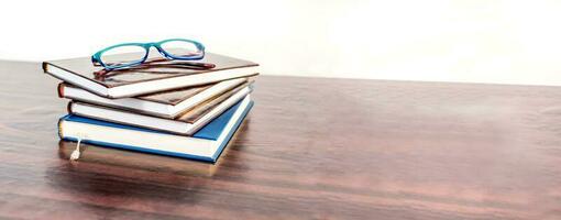 Stack of books with reading glasses on wooden desk. Education banner. photo