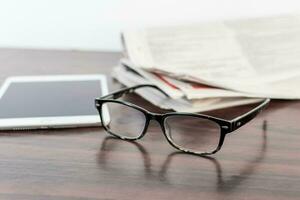 Newspaper and reading glasses on wooden table. photo