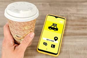 Coffee mug to go and smart phone with app, on wooden desktop. Get taxi app. photo