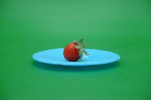 a strawberry on a blue plate. strawberry isolated green background. photo