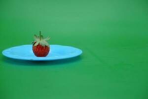 a strawberry on a blue plate. strawberry isolated green background. photo