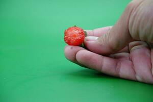 hand holding a bitten strawberry isolated on green background. photo