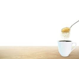 A spoonful of granulated sugar is poured into a white coffee mug placed on a wooden floor. photo